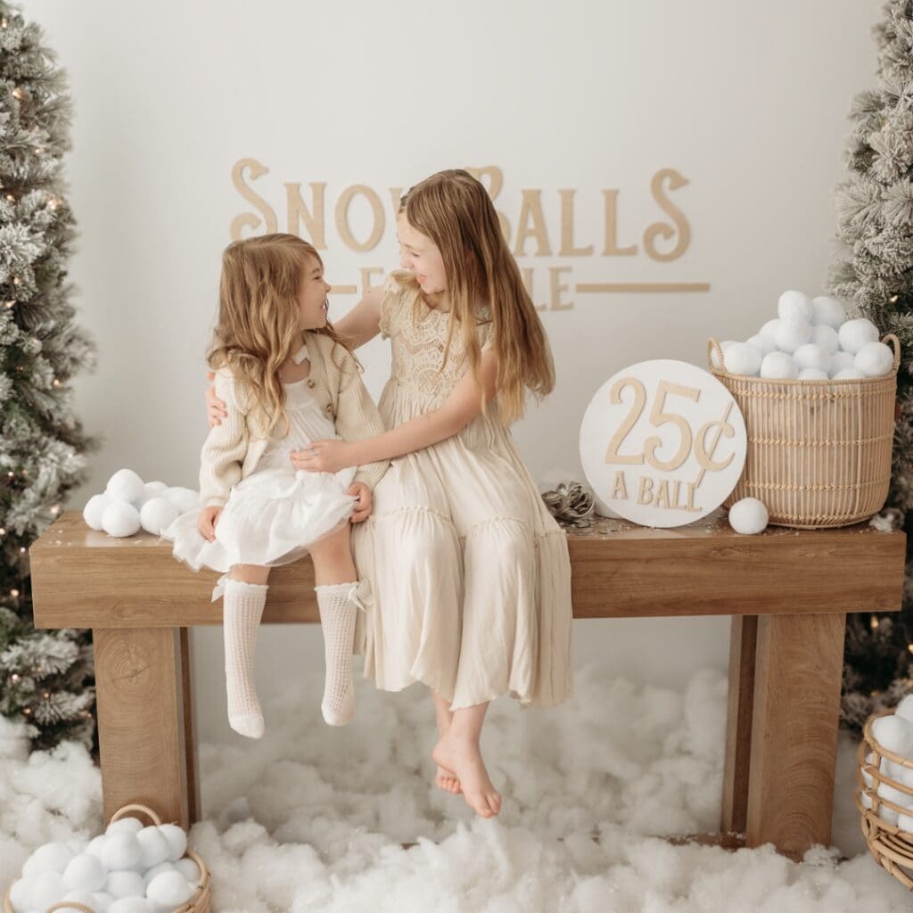 Two young girls enjoying a snowball-themed mini photo session in a festive setting.