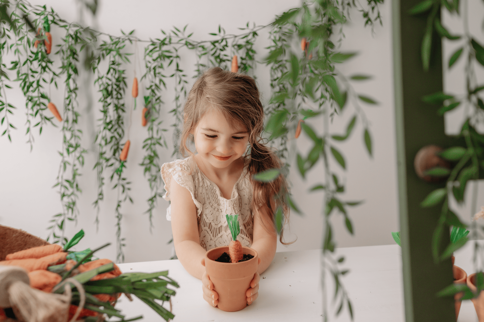 Easter mini session with a young girl holding a potted plant, surrounded by greenery and festive dec.
