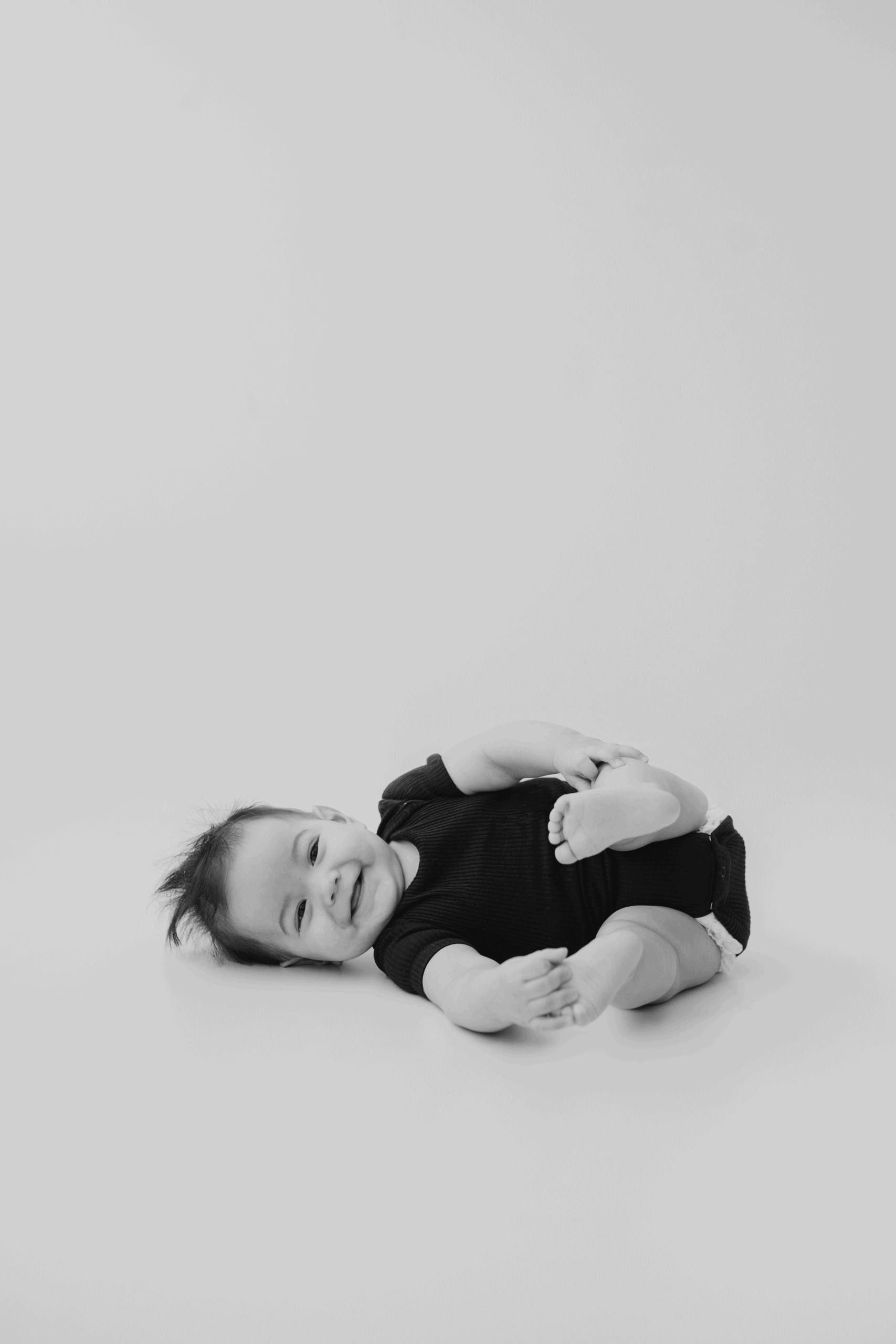 Baby lying on the floor smiling, in a black outfit, in a professional studio setting.